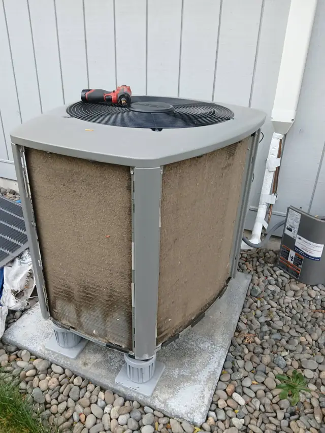 Before: the condenser's coil faces matted brown with cottonwood, a drill on the fan guard